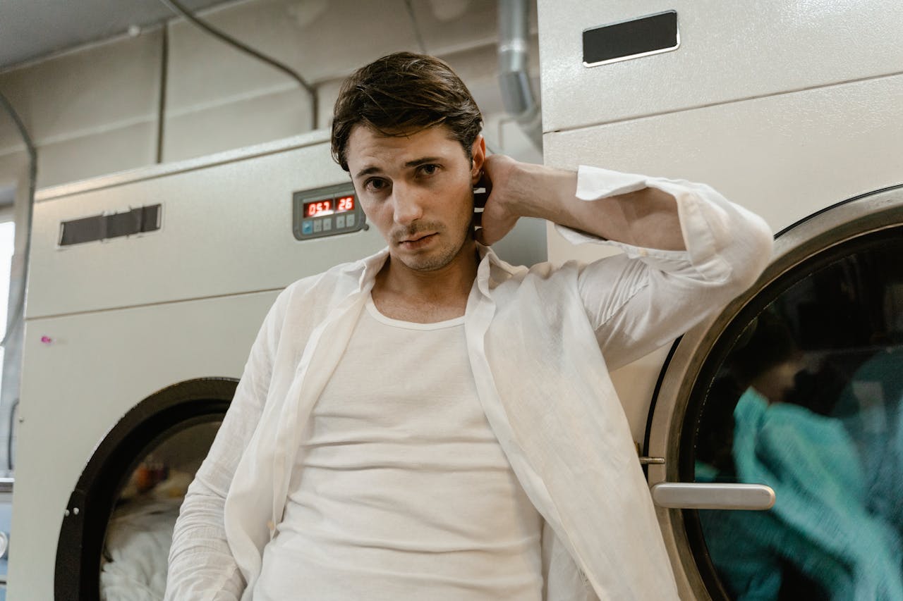 portfolio-06 Young man in a white shirt leaning on a washing machine in a laundry facility.